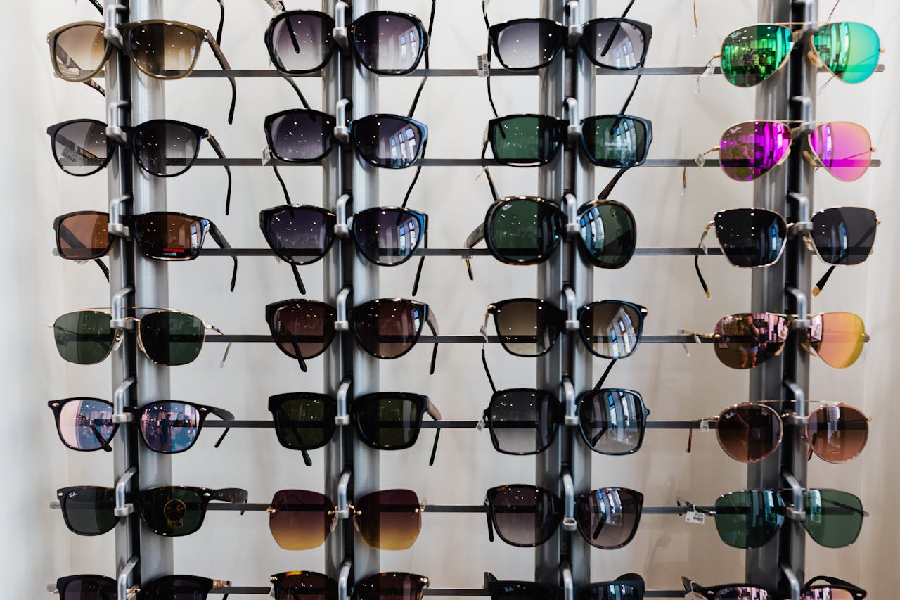 gallery-03 Variety of sunglasses displayed on racks in an indoor eyewear shop setting.